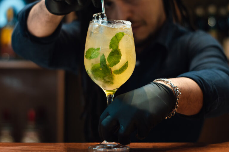young bartender man, with a mixer, preparing a drink with rum, orange juice and mint in a nightclub, bar concept.